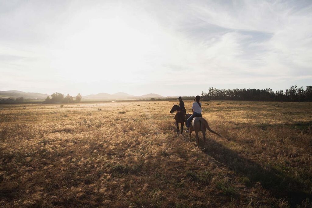 2 women ride horseback through the fields of colorado