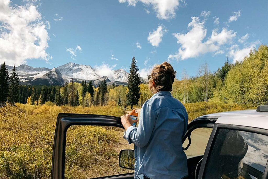 a woman looks out at the mountains flanked with dark green pines, and yellow leaved aspens