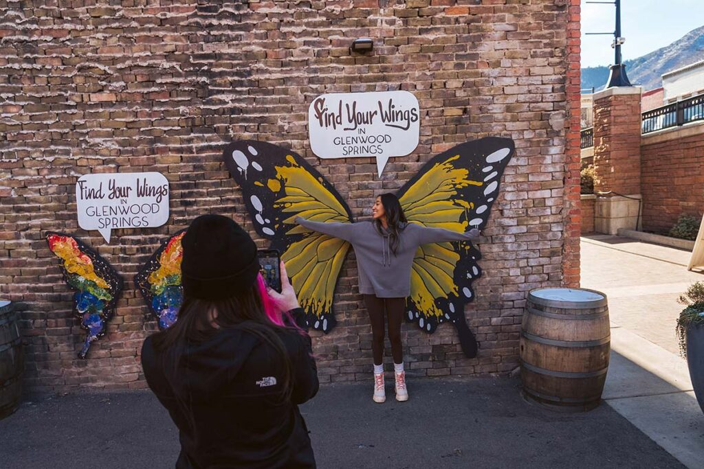 Woman standing in front of a butterfly mural that reads "Find Your Wings in Glenwood Springs"