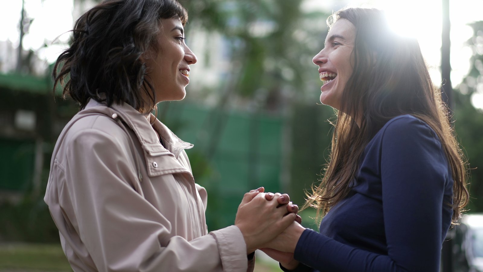 Two women smile and clasp hands outdoors in a moment of mutual support